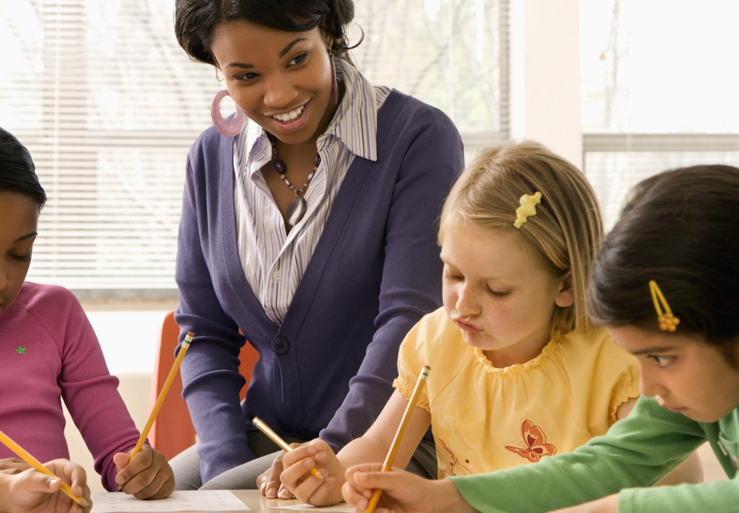 一位女教师正在指导三名小学生在餐桌上写字